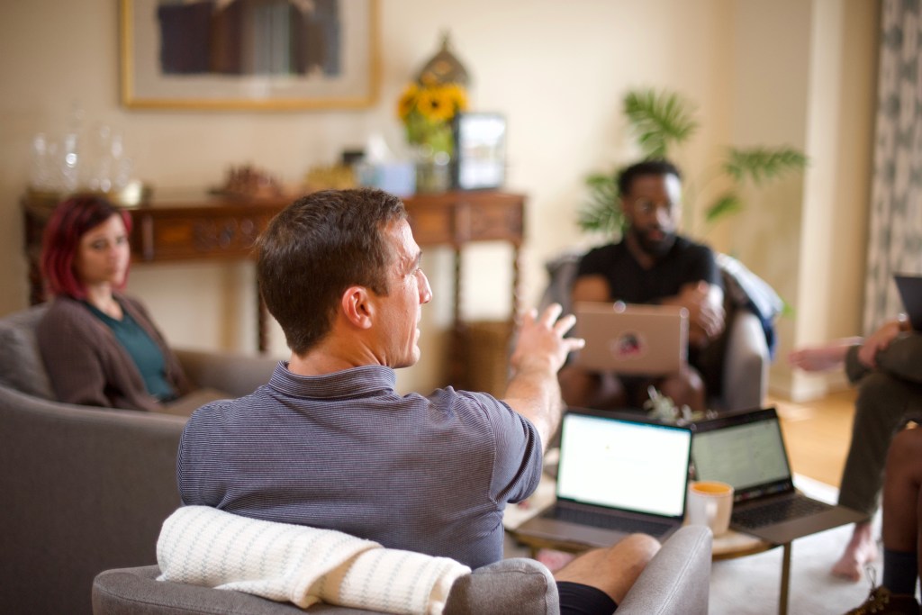 Team working together around a living room, with others joining remotely