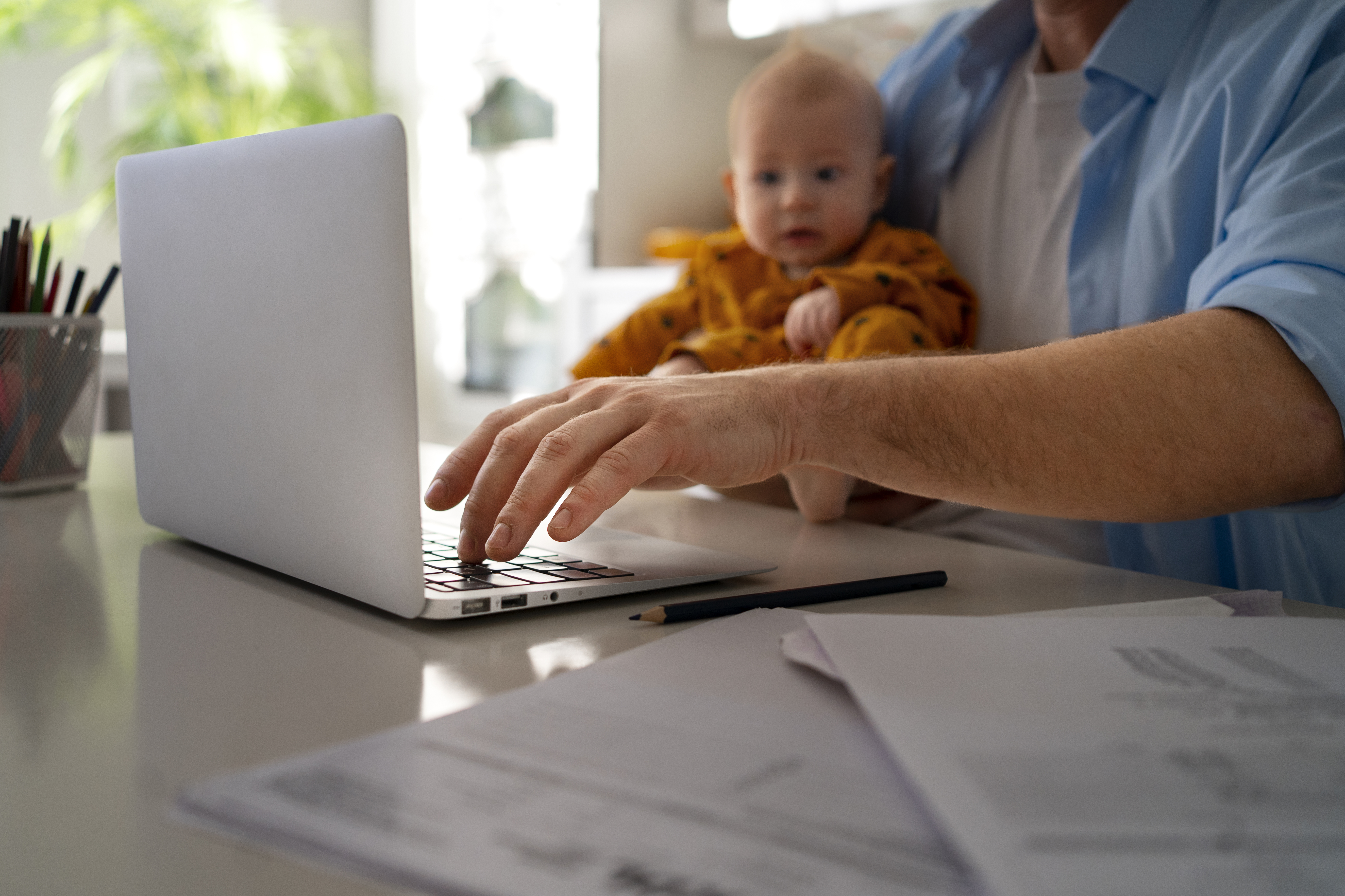 a parent at work at home on their laptop holding a baby