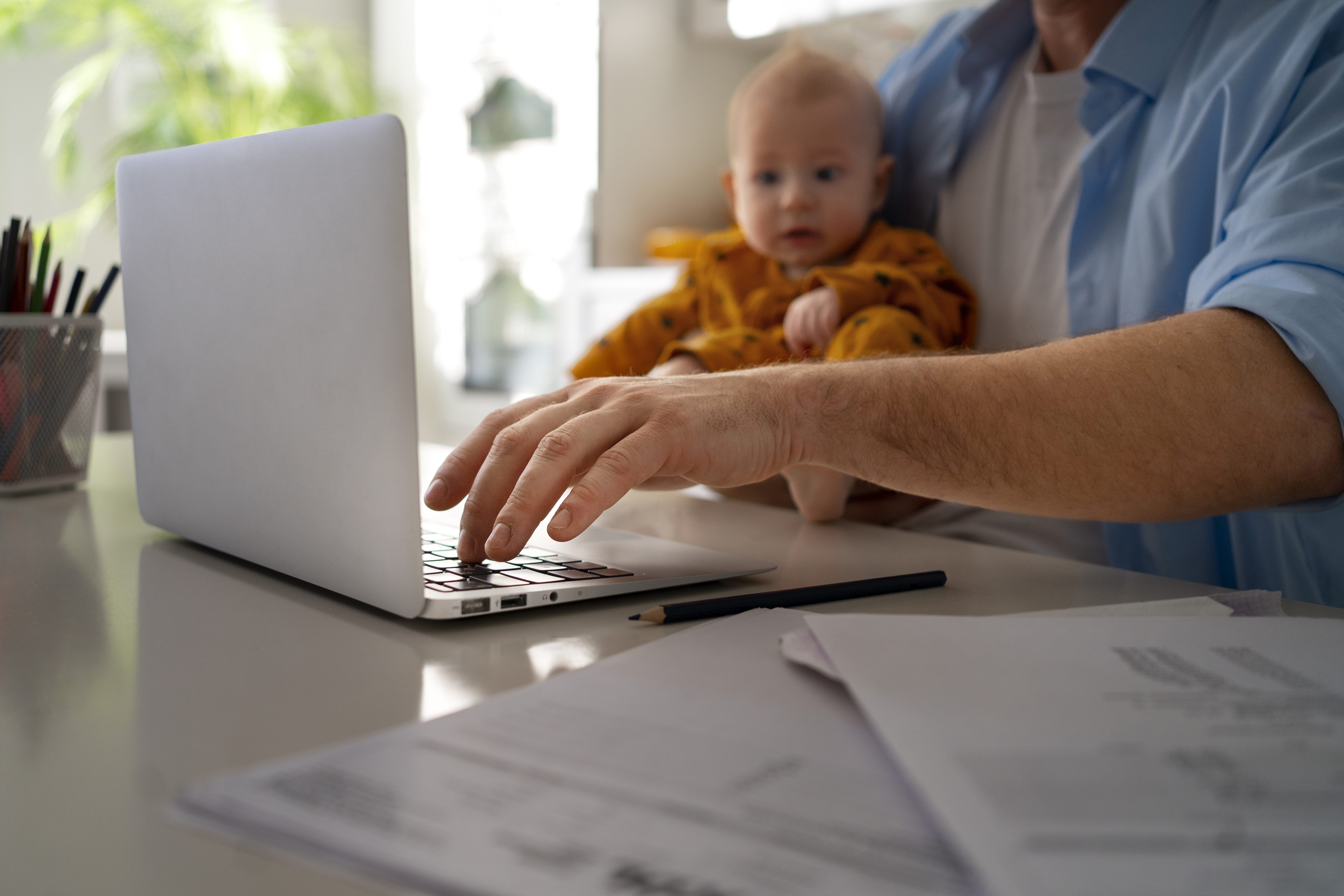working-parents a parent at work at home on their laptop holding a baby