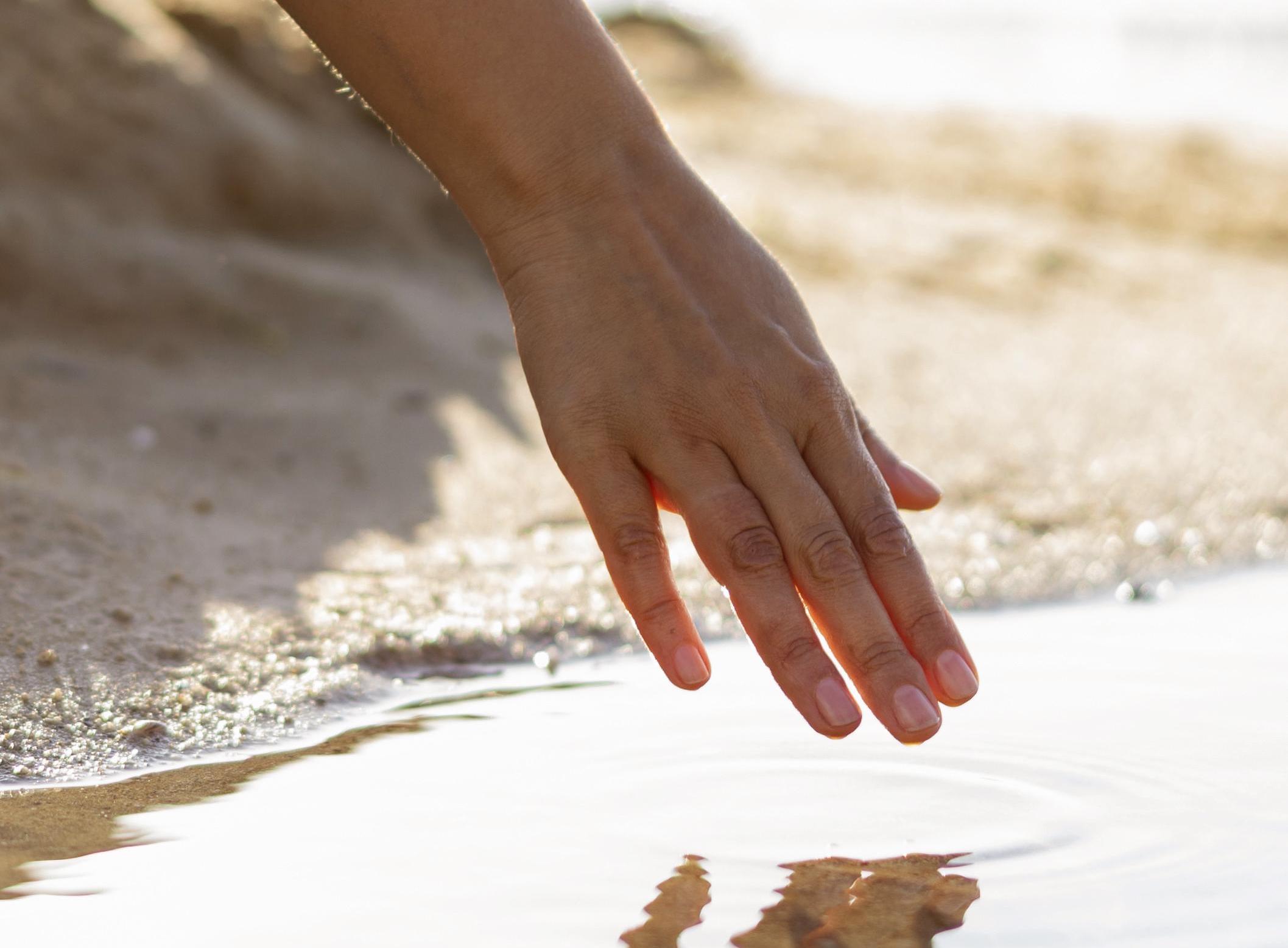 woman-running-her-hand-through-water-beach